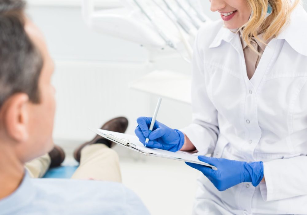 Female doctor recording diagnosis while consulting with patient in modern dental clinic